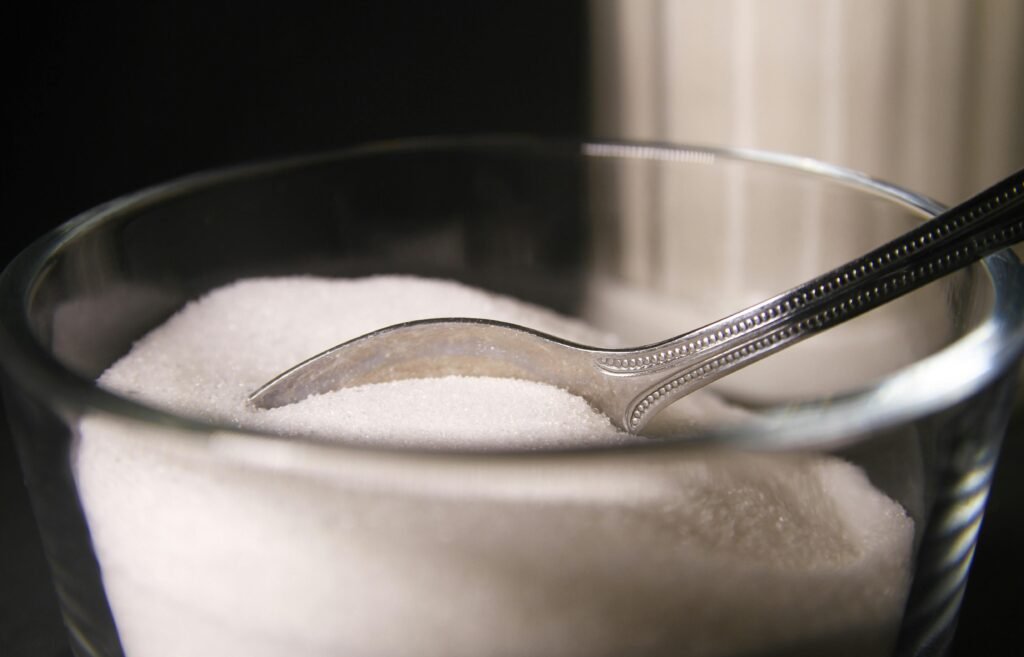 Detailed shot of granulated sugar in a glass bowl featuring a spoon.